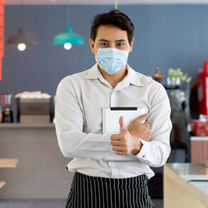 A man in a mask holding a pad of paper with arms crossed, he appears to be a waiter in a restaurant
