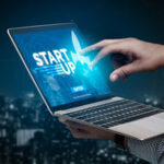 Laptop computer with the words "start up" on the screen and a hand pointing to it