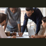 Group of professionals standing around a table, looking down working on a project