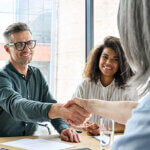 Happy businessman and businesswoman shaking hands at group board meeting.