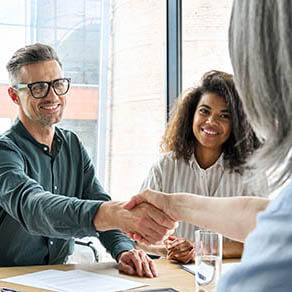 Happy businessman and businesswoman shaking hands at group board meeting.