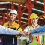 Employees in construction gear smiling with hands extended