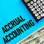 Words "Accrual Accounting" on a blue background next to cash and a calculator