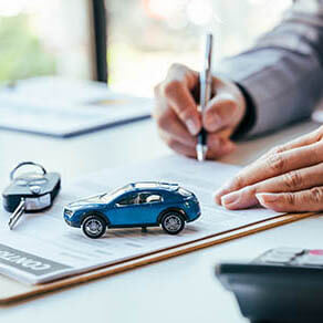 Man signing car insurance document or lease paper. Writing signature on contract or agreement. Buying or selling new or used vehicle. Car keys on table. Warranty or guarantee. Customer or salesman.
