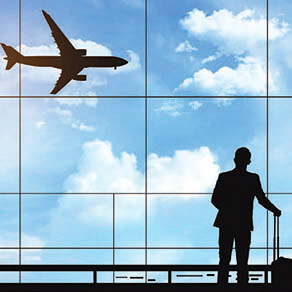 Business man with luggage looking out window at airplane landing