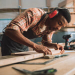 Man, wearing noise cancelling headphones, working on a project at wood working bench