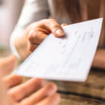 Close up of someone handing someone a check