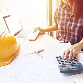 Woman using calculator at a desk with hard hat nearby