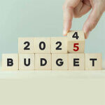 Hand flips wooden cube and changes the inscription "BUDGET 2024" to "BUDGET 2025" with grey background, copy space