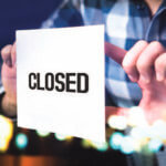 Person holding up sign reading “CLOSED”