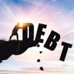 Silhouette of man pushing the word "DEBT" off a cliff