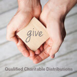 Hands holding block with the word "give" written on it and Qualified Charitable Distributions written underneath