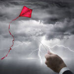A red kite flying in a lightening storm with a hand reaching up to the storm holding the kite string