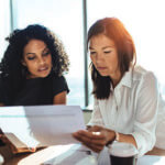 Two women in front of a window looking over documents