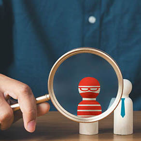 businessman holding magnifying glass up to a small wooden toy of a 