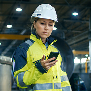 Female Industrial Worker in the Hard Hat Uses Mobile Phone While Walking Through Factory