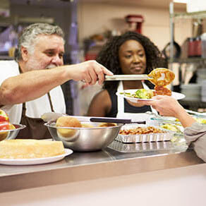 Kitchen with two people Serving Food In Homeless Shelter