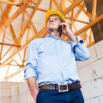 Senior architect with smartphone at the construction site.