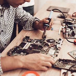 Manufacturing tech with soldering tool working on technical equipment on a table