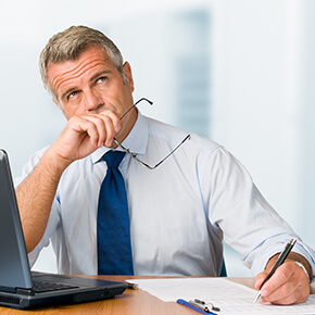 Man thinking while sitting at laptop holding glasses and writing