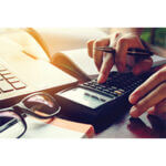 Person using calculator with open book and laptop