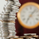 Stack of coins with blurred clock in background