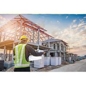 Construction site with a man with a safety hat and safety vest looking at blue prints