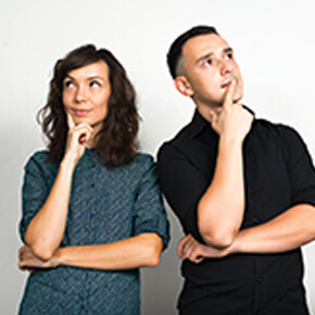 A lady and man standing with their finger on their chin looking up in thought