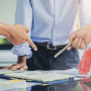 Contractor and engineer with blueprints standing at a desk in a discussion