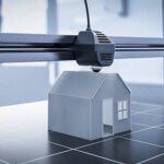 Black & white photo of a miniature house being made by a 3-D printer