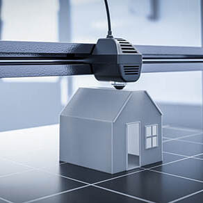 Black & white photo of a miniature house being made by a 3-D printer