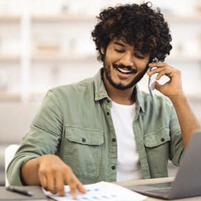 Young man on phone; smiling and looking at graphs.