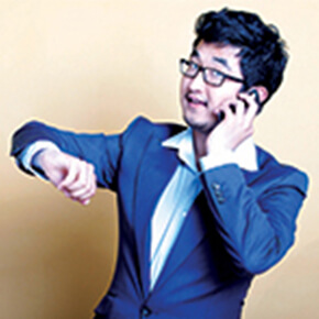 Man holding a cell phone, dressed in a blue suit holding his arm up where his watch is