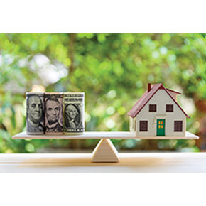 Scale with dollar bills on one side and a house figure on the other side