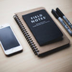 Two notepads one saying Field Notes and two black markers and one cell phone
