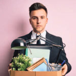 Man in suit holding box containing items from an office desk