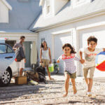 A family of four on vacation. The parents are unloading their luggage while the children, a boy and a girl, are playing with a bleach ball.