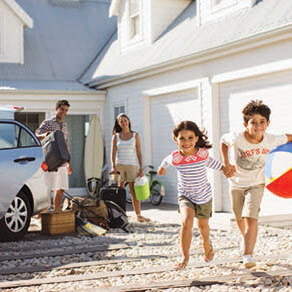 A family of four on vacation. The parents are unloading their luggage while the children, a boy and a girl, are playing with a bleach ball.
