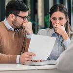 Portrait of a couple with financial problems looking at document in financial adviser's office.