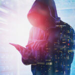 Person in zip up hooded sweatshirt on tablet with coding faded in front of him