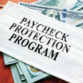 Medical mask with Paycheck Protection Program written on it sitting on top of $100 dollar bills