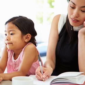 Woman writing in book with young child sitting next to her