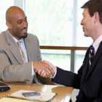 Two business men sitting at a table shaking hands