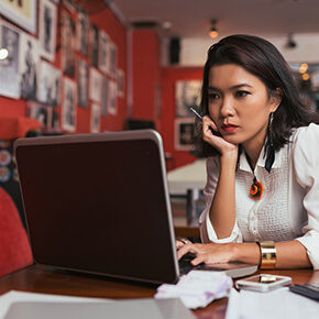 A lady sitting at a table looking at a computer laptop, room painted red with pictures on the wall