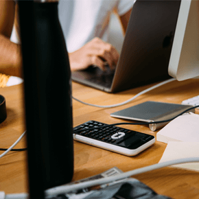 Someone sitting at a desk working on laptop with phone on desk
