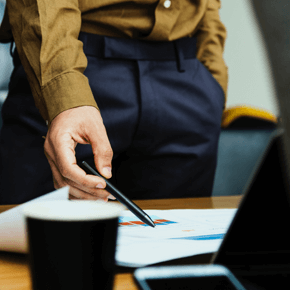 Person standing pointing with a pen down on charted paper