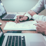 Two people with two laptops and looking over papers