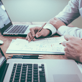 Two people with two laptops and looking over papers